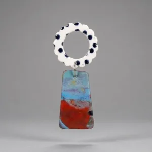 Close-up of flower earrings with a white scalloped ring top with black dots and a marbled blue-red trapeze drop on a light grey background.