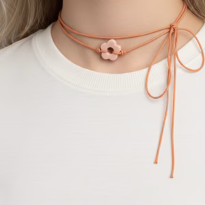 Macro close-up of a 1.5cm peach-toned polymer clay flower charm with a satin finish, knotted onto a double-strand terracotta cord.