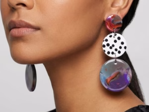 Woman wearing abstract sculptural earrings featuring a marbled stud and a large marbled and white and black polka dot drop.